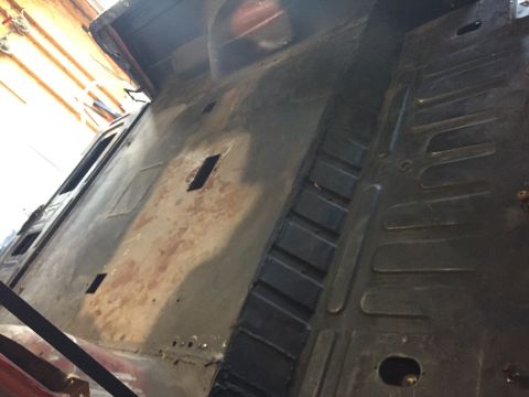 Photo of a bare metal vehicle floor pan and bed during restoration