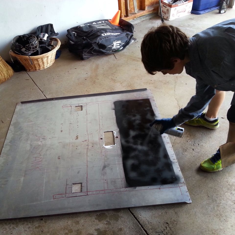 Person applying black coating to a large metal floor panel