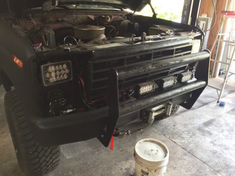 Front of a black Ford truck with grille guard and LED light bars in a garage