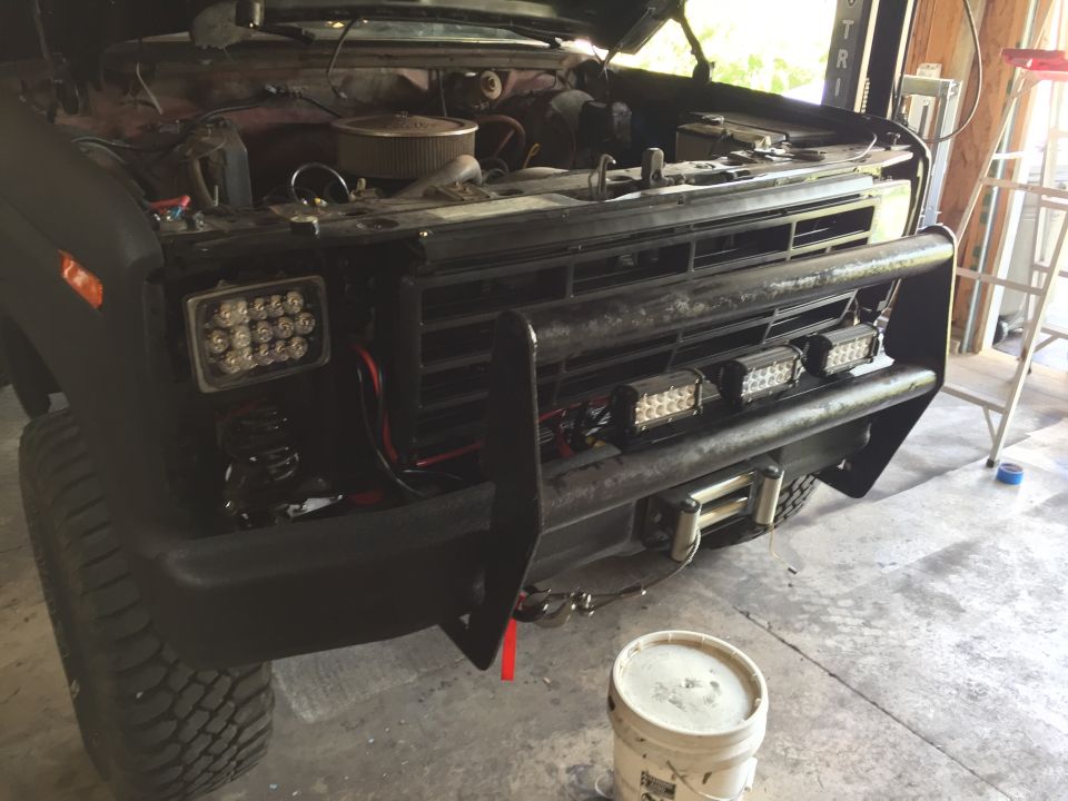 Front of a black Ford truck with grille guard and LED light bars in a garage