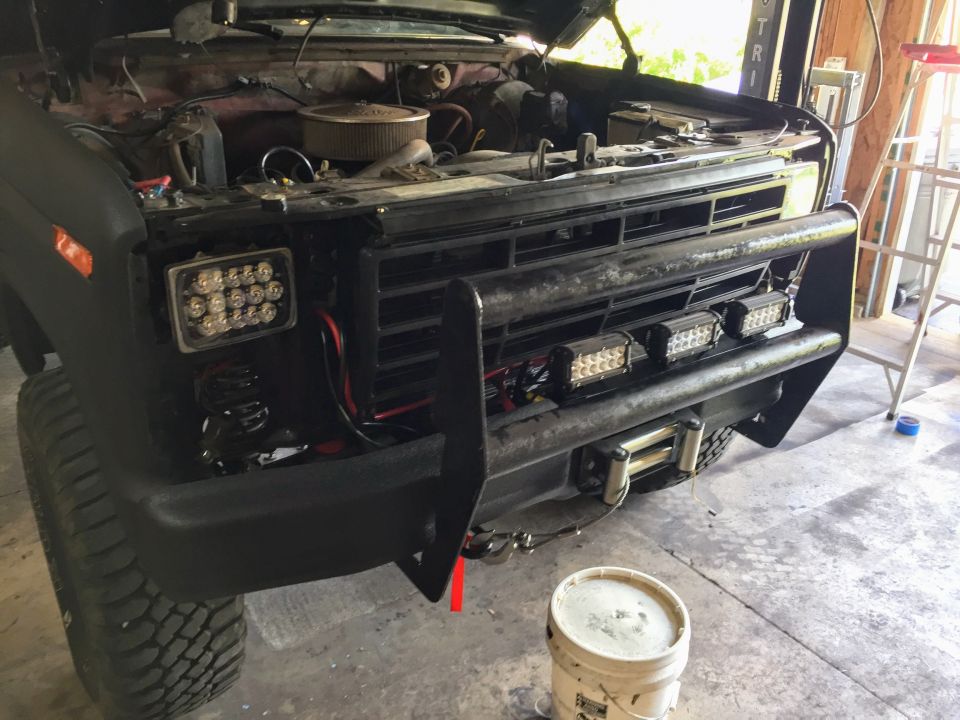 Front of a black Ford truck with grille guard and LED light bars in a garage