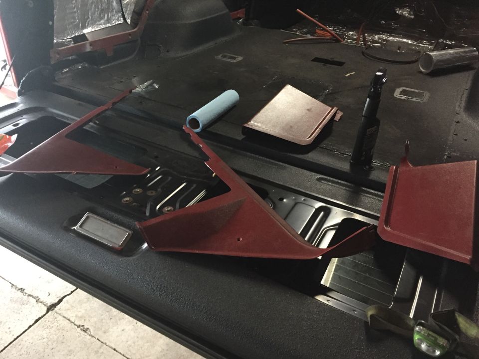 Red sheet-metal floor brackets laid on a bare vehicle floor pan