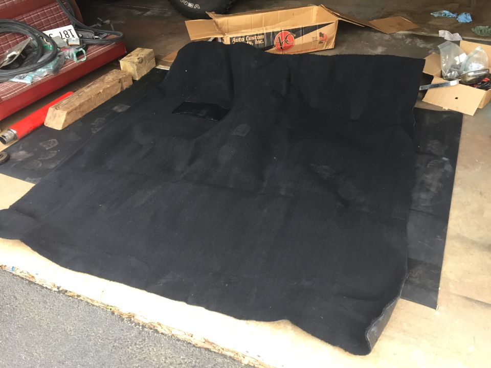 Black molded automotive carpet laid out on a garage floor