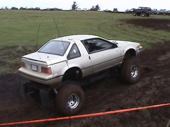 Silver 1980s sports coupe sitting on huge mud tires and a lift kit on a dirt course