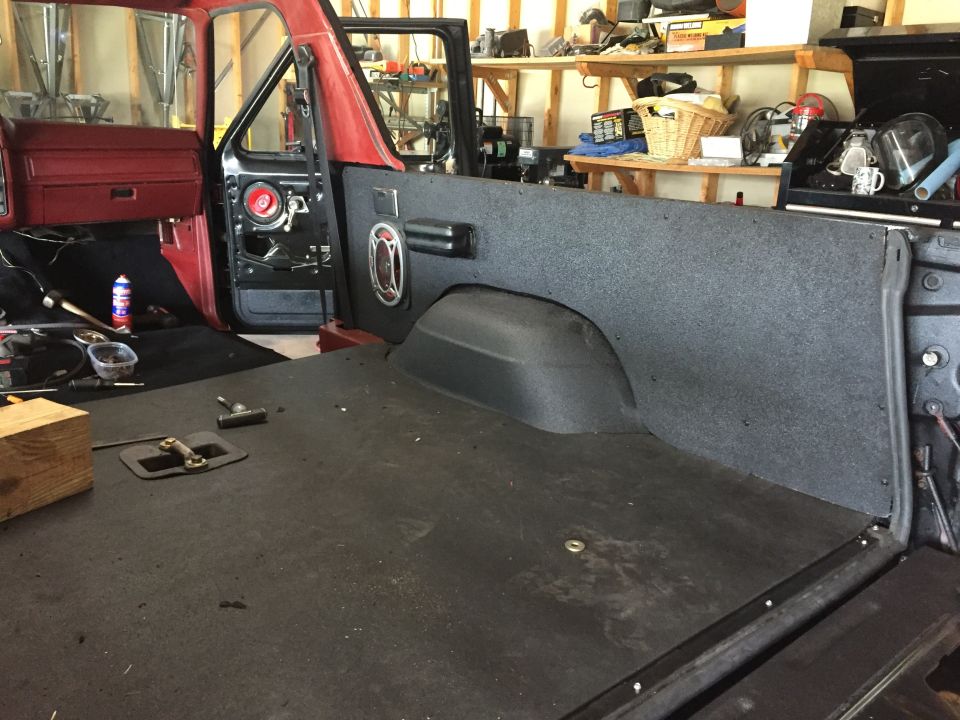 Interior of a red Ford Bronco with driver's door open, showing black carpet and bed lining.