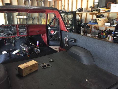 Interior of a red and black Ford Bronco with doors removed, tools on the floor.