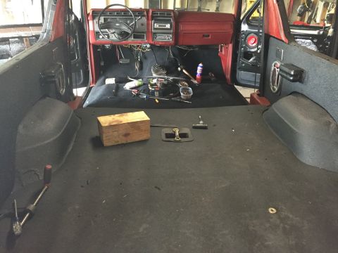 Interior of a red Ford Bronco with carpet removed, showing dashboard and tools on the floor.
