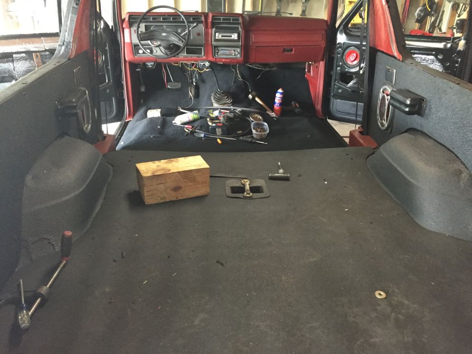 Interior of a red Ford Bronco with carpet removed, showing dashboard and tools on the floor.