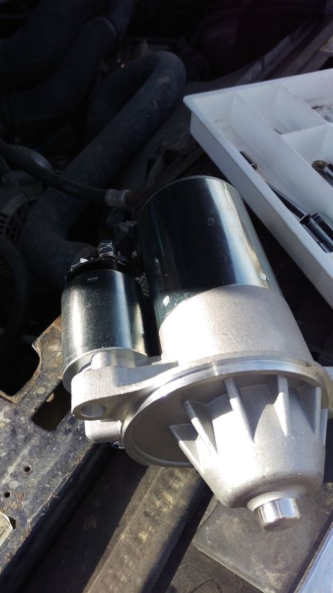 1994 Ford Bronco - Photograph of a new gear-reduction starter motor next to its mounting location in the engine bay.