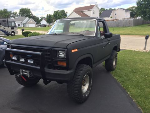 Matte black lifted 1980s Ford Bronco with bull bar and LED lights.