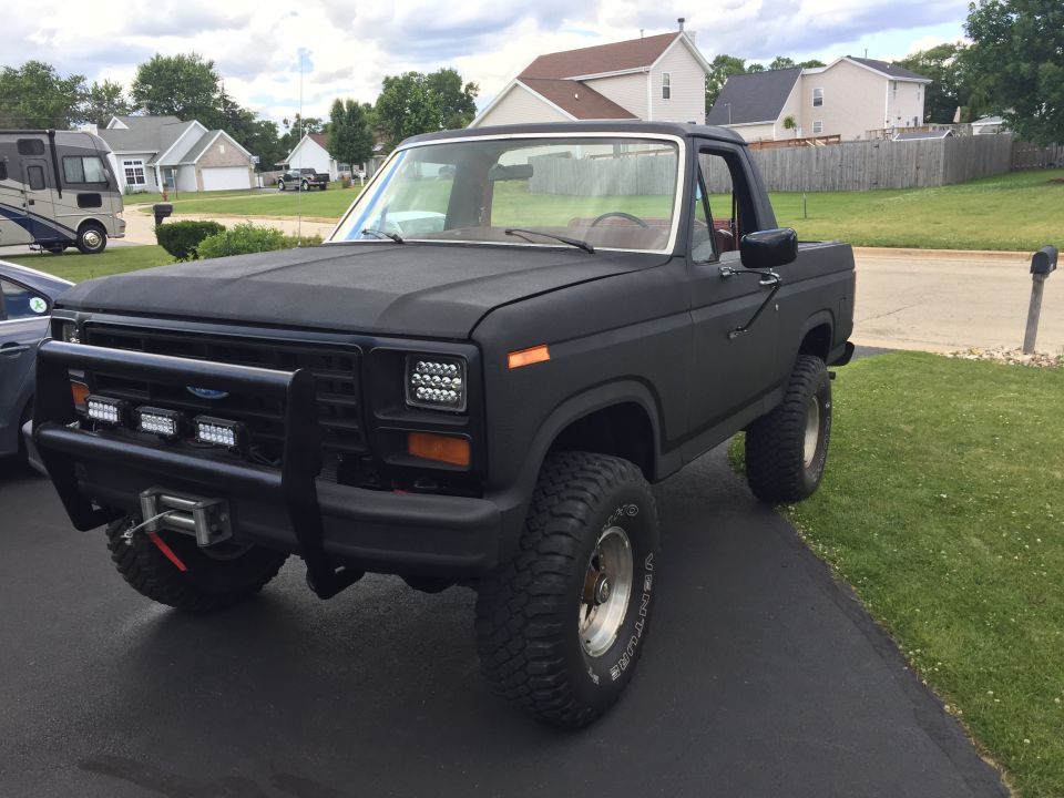 Matte black lifted 1980s Ford Bronco with bull bar and LED lights.