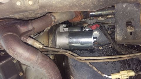 1994 Ford Bronco - Underbody photograph of a starter motor installed near the exhaust pipes and transmission.