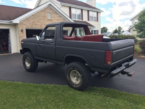 Matte black lifted 1980s Ford Bronco, rear 3/4 view, with red interior.