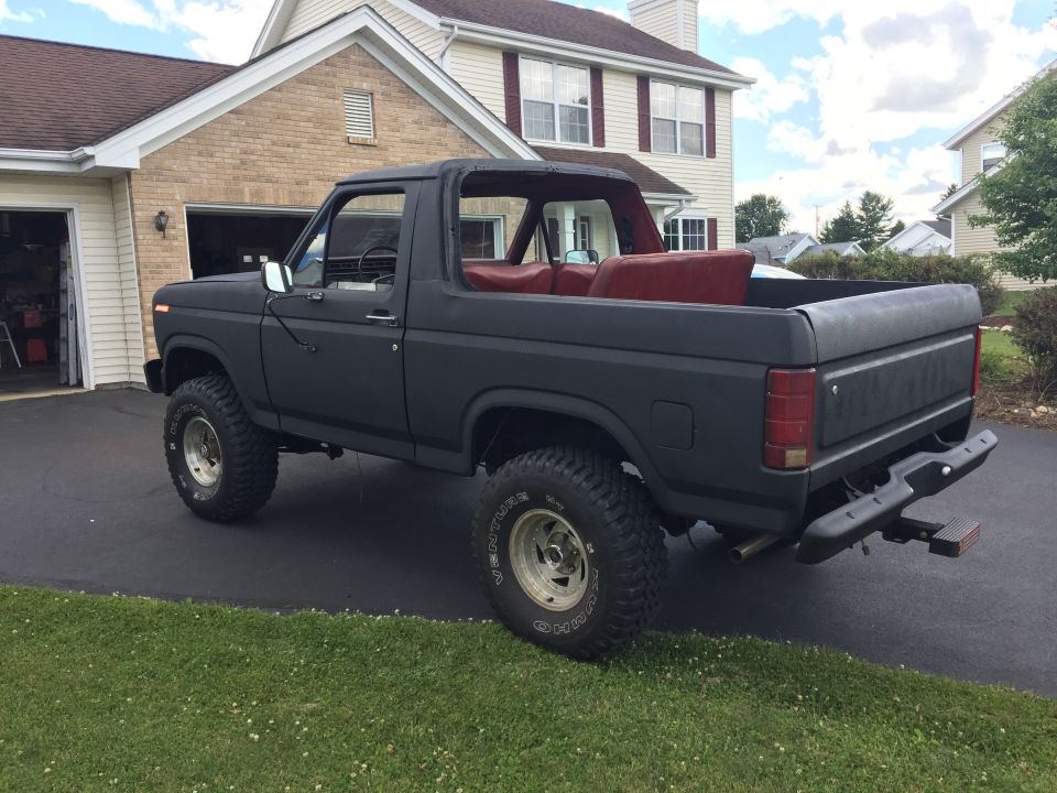 Matte black lifted 1980s Ford Bronco, rear 3/4 view, with red interior.