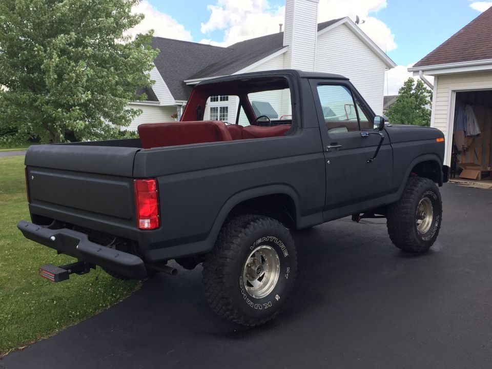 Matte black 1980s Ford Bronco with red interior, parked on a driveway.
