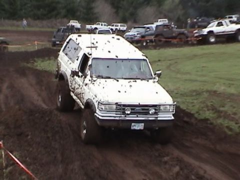 1989 Ford Bronco - White 1989 Ford Bronco navigates a muddy course, with other trucks and SUVs visible in the background.