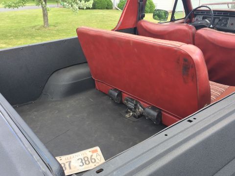 Interior of a classic Ford Bronco showing red rear seats and black cargo area with Illinois license plate.