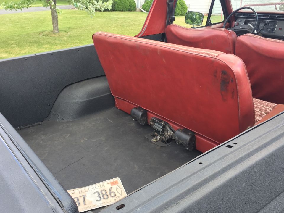 Interior of a classic Ford Bronco showing red rear seats and black cargo area with Illinois license plate.