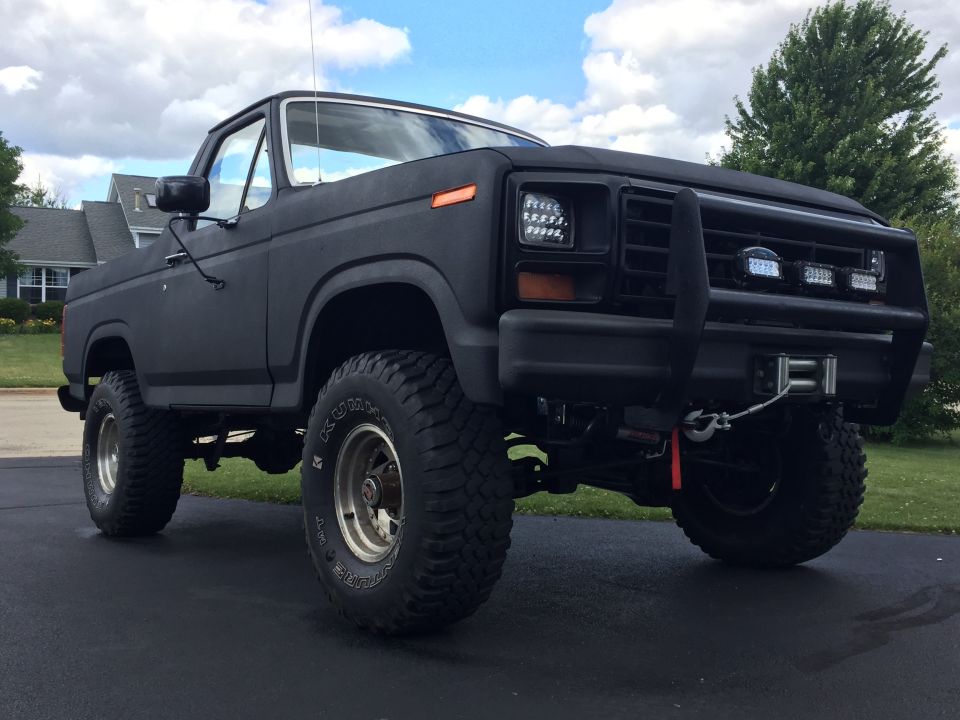 Matte black 1980s Ford Bronco with off-road tires, bull bar, and winch.