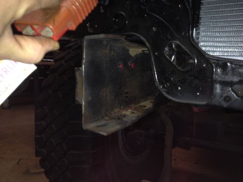Orange wheel chock near black vehicle frame, tire, and radiator.