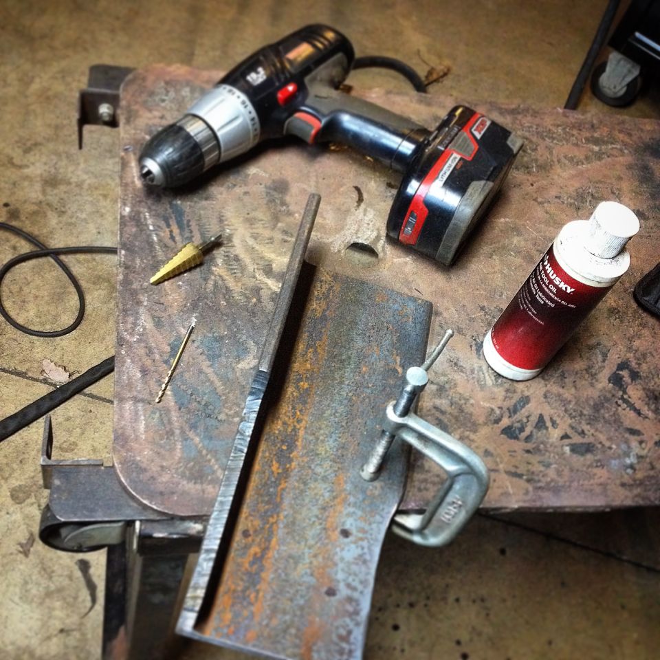 Cordless drill, drill bits, metal, clamp, and tool oil on a workbench.