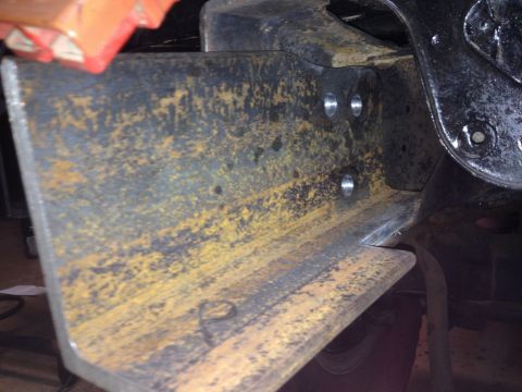 Close-up of a rusted steel bracket with two sets of pre-drilled holes, part of a vehicle frame.