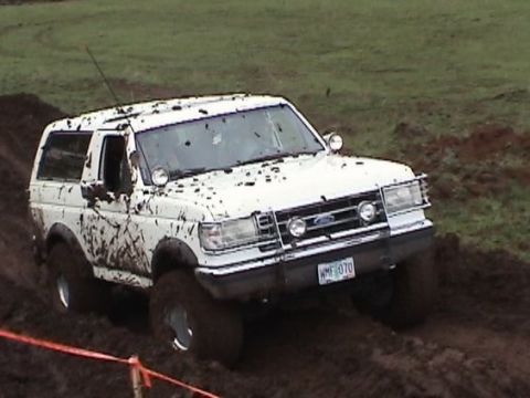 1989 Ford Bronco - This Ford Bronco is navigating a challenging muddy terrain, kicking up dirt as it goes.