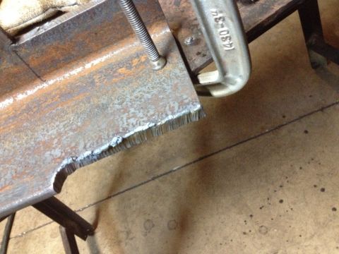 Metal beam with rough cut edge secured by C-clamp with text
