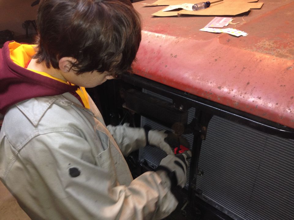 Person reaching behind a red truck front clip to work on the radiator and grille