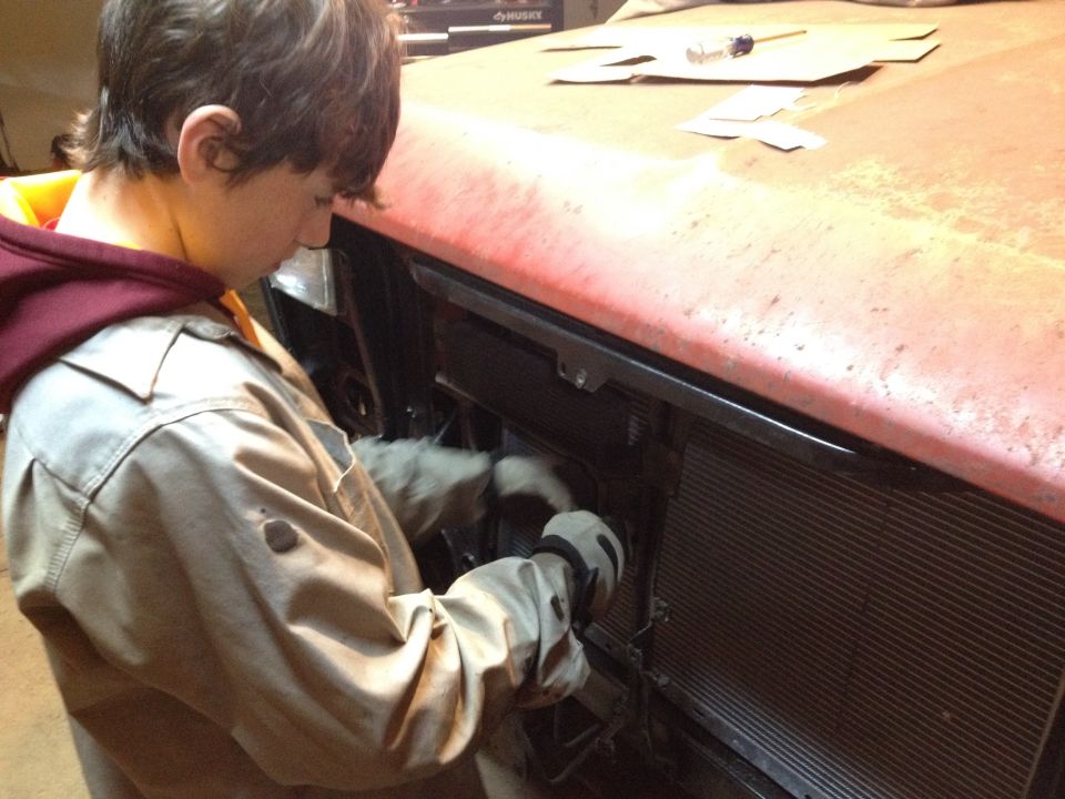 Person working behind a red truck front clip near the grille and radiator