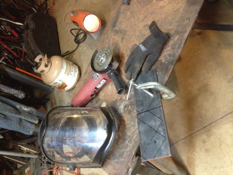 Angle grinder, welding helmet, torch and cut metal pieces on a steel workbench