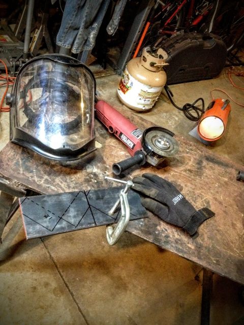 Welding helmet, angle grinder, torch and cut metal bracket on a workbench
