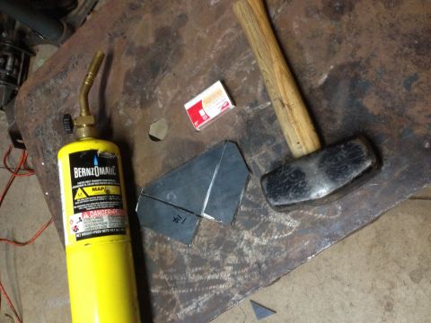 BernzOmatic torch, sledge hammer and folded metal bracket on a steel bench