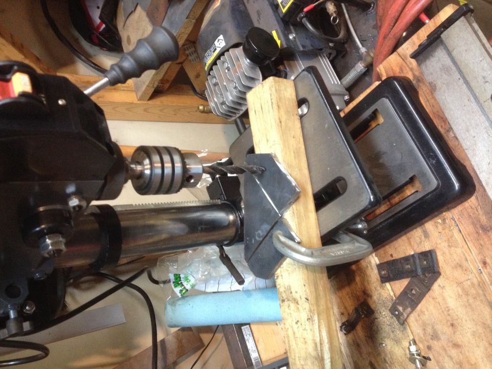 Drill press and clamp holding a fabricated metal bracket in a workshop