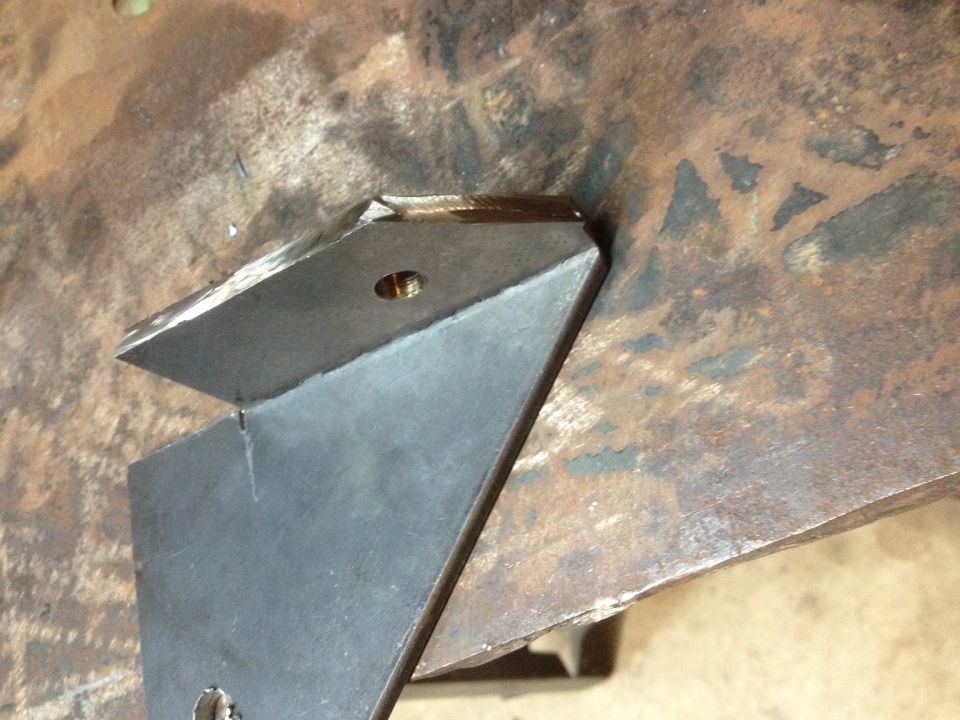 Welded angular metal bracket sitting on a rusty steel surface