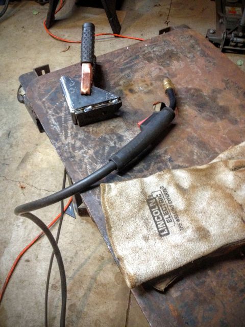 Welding electrode holder and ground clamp with Lincoln leather glove on a bench