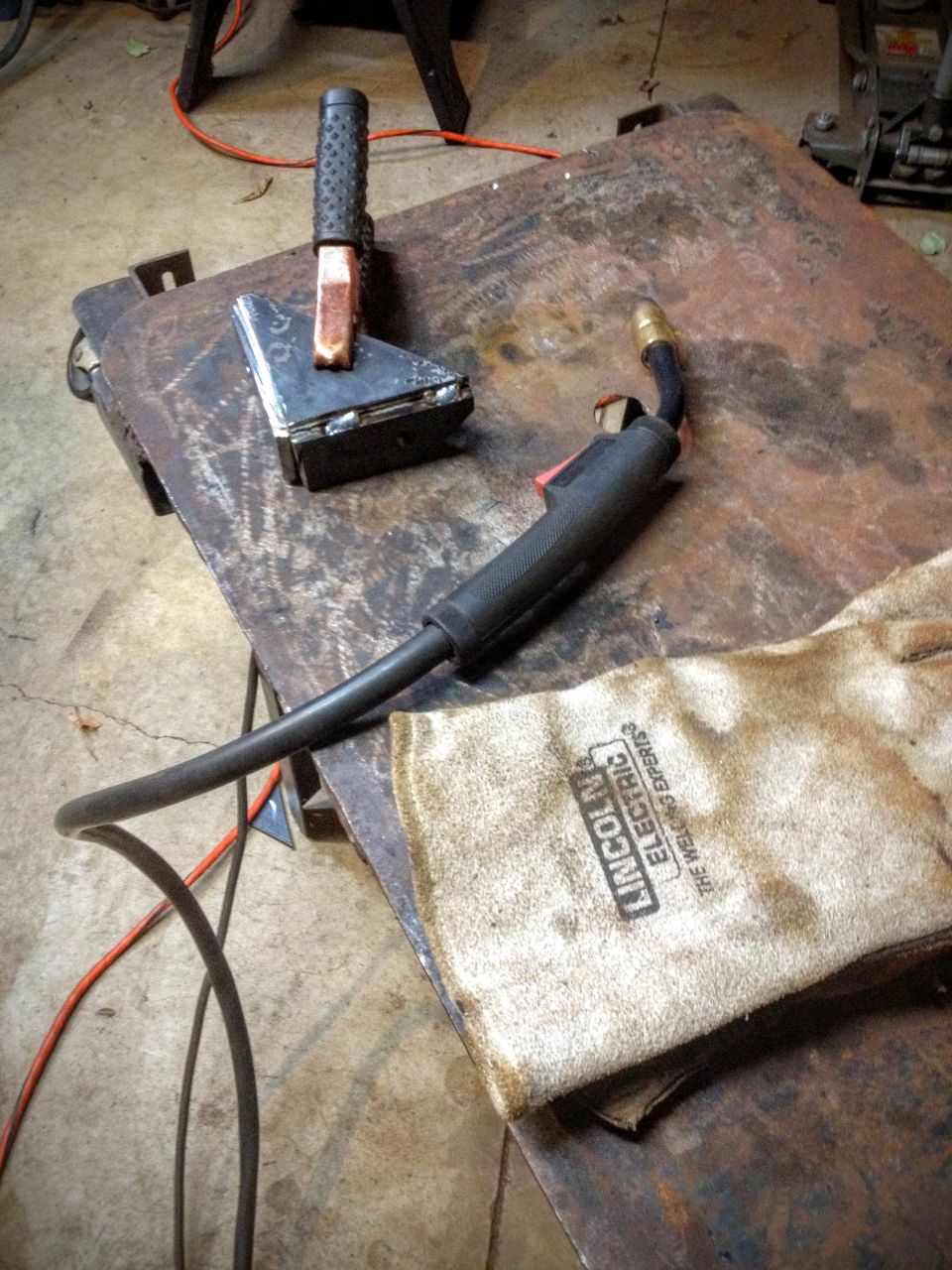 Welding electrode holder and ground clamp with Lincoln leather glove on a bench