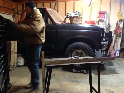 Man working on a black Ford Bronco in a garage with a folding workbench