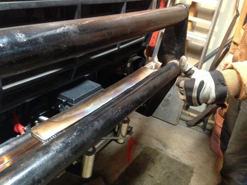 Gloved hand fitting a fabricated tubular bumper or bar to a vehicle front end