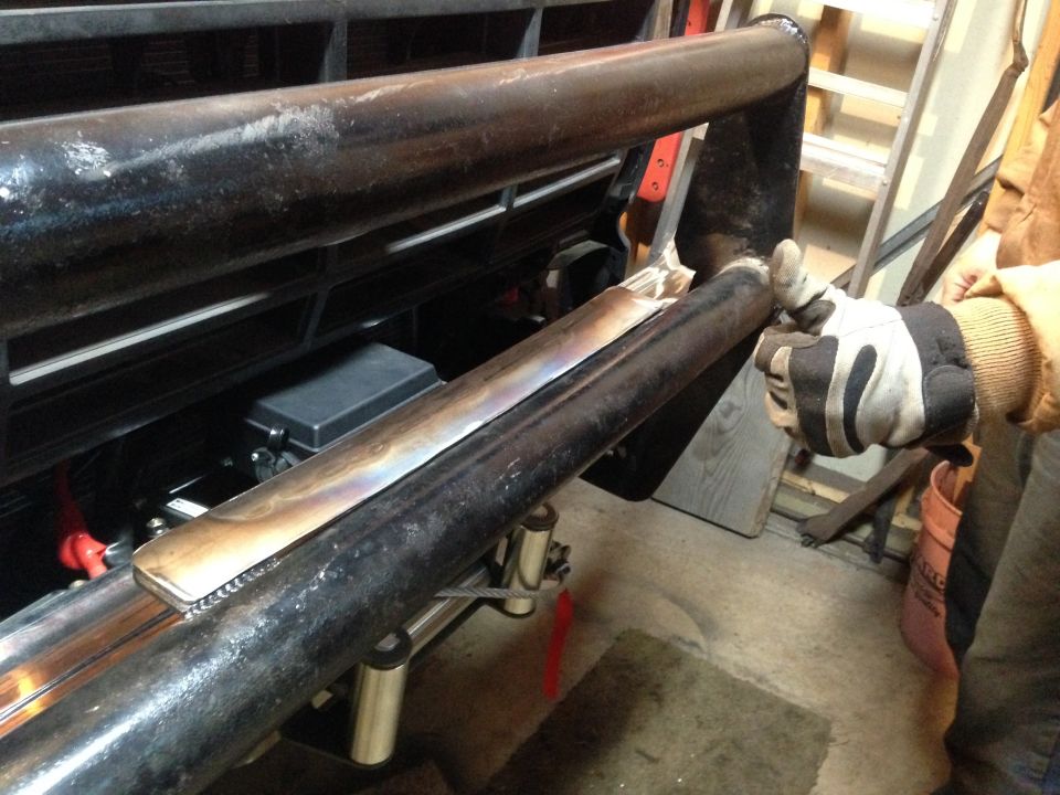 Gloved hand fitting a fabricated tubular bumper or bar to a vehicle front end