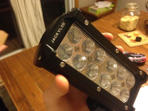 Hand holding a JackLED LED light bar over a wooden table
