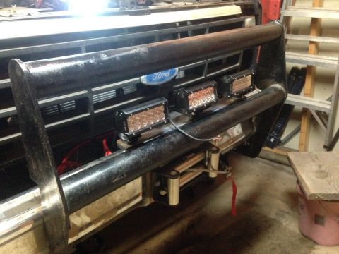 Ford truck front grille with bull bar and three mounted LED light bars in a garage
