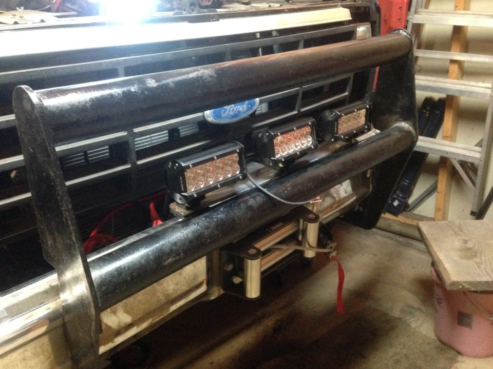 Ford truck front grille with bull bar and three mounted LED light bars in a garage