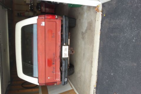 Rear view of a red Ford Bronco with white top parked in a garage