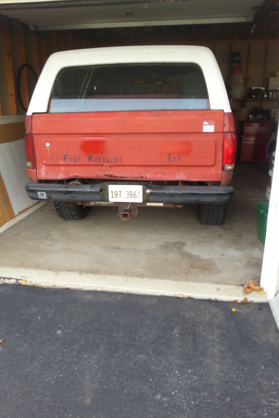 Rear view of a red Ford Bronco with white top parked in a garage
