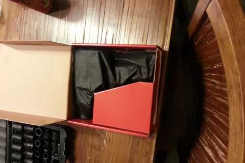 Open red product box containing a black tool, on a wood table