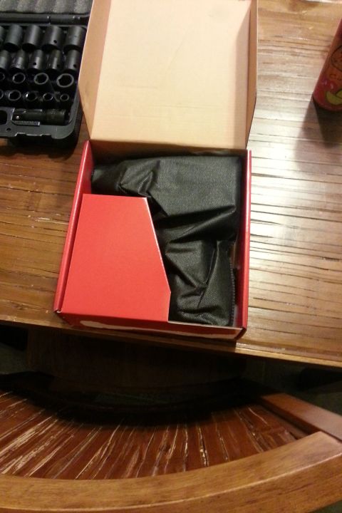 Open red product box containing a black tool, on a wood table