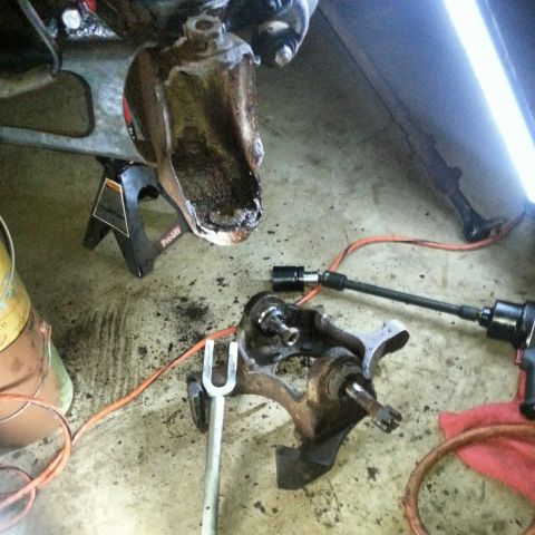 Front axle steering knuckle and components on a garage floor with impact tools
