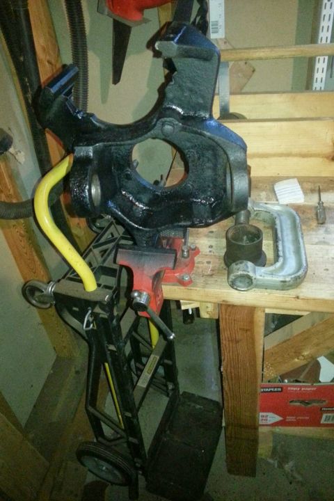 Black painted steering knuckle in a vise above a hand cart in a garage
