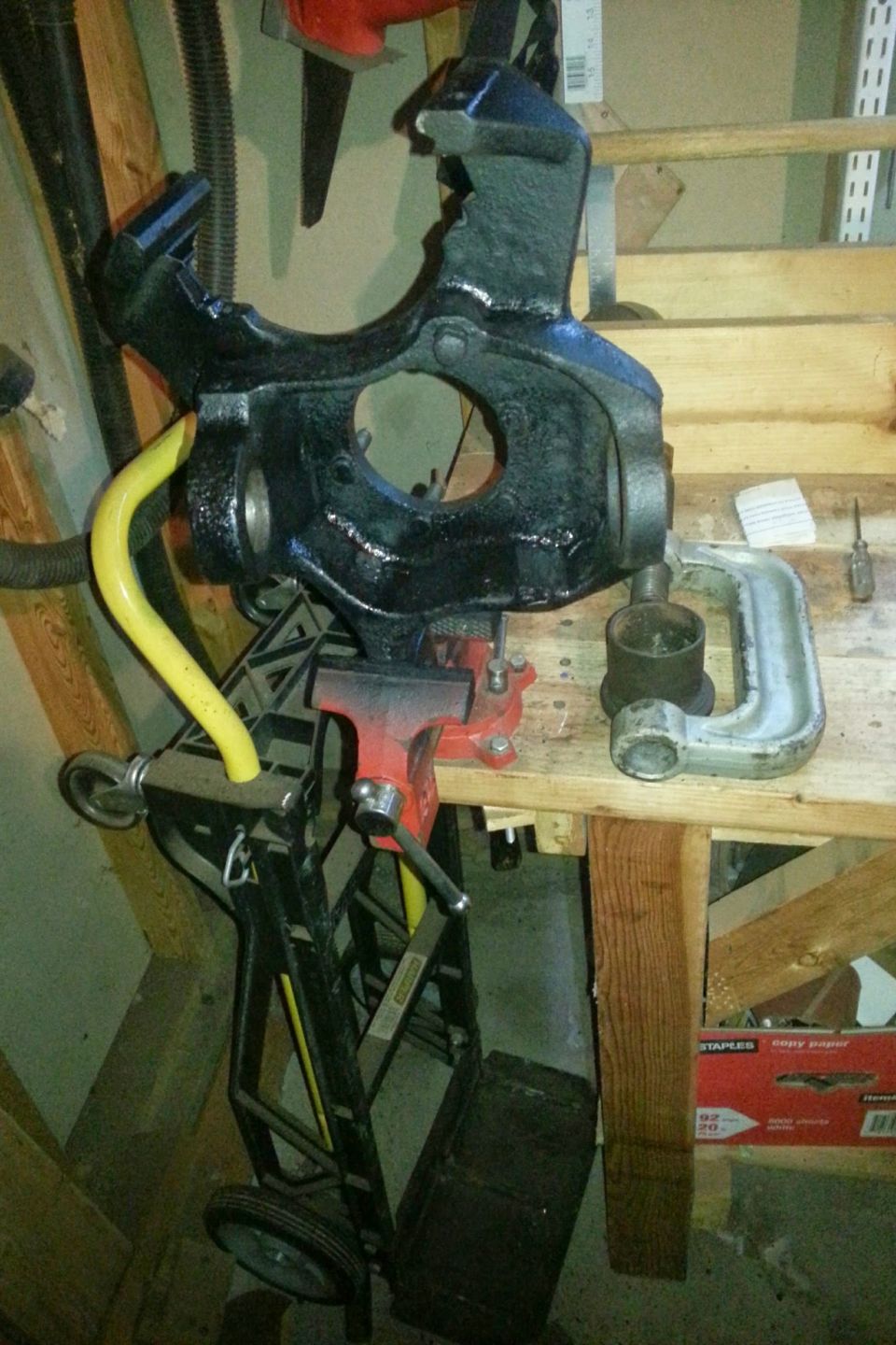 Black painted steering knuckle in a vise above a hand cart in a garage